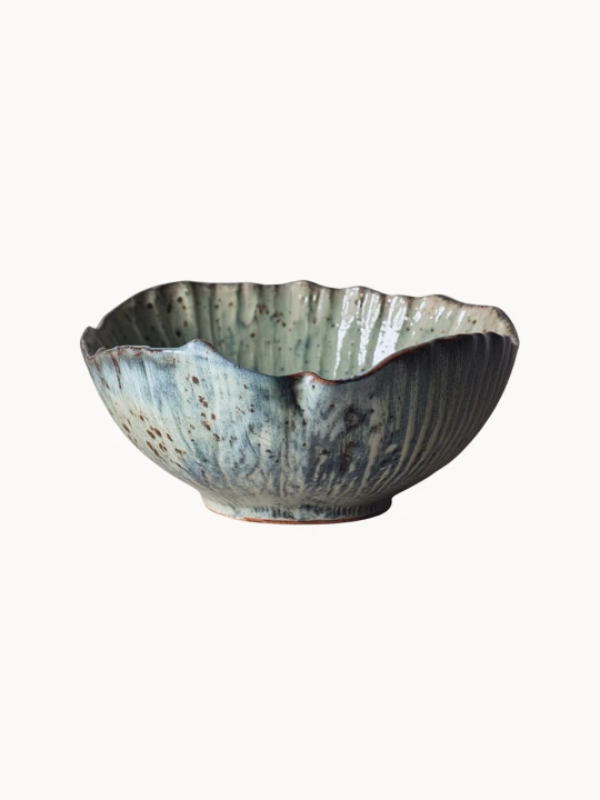 A rustic ceramic bowl with a mottled light blue and beige glaze with brown speckled details, on a plain white background.