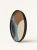 A large ceramic plate with a black rim features an abstract design of color blocks in brown, beige, light blue, and black. The plate is shown standing upright at a slight angle on a solid white background.