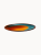 A flat ceramic plate with a vibrant, artistic glaze with a fiery orange center bleeding into a deep teal border.