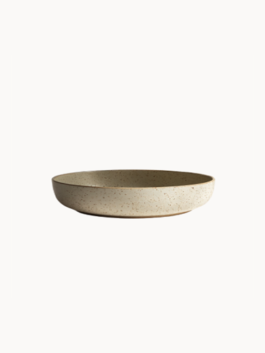 A shallow, round ceramic bowl with a speckled beige and light grey texture, on a plain white background.