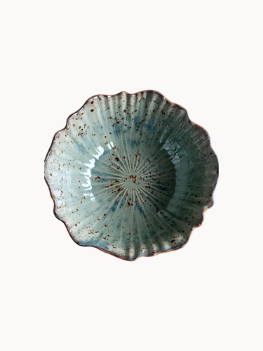 A top-down view on a rustic ceramic bowl with a mottled light blue and beige glaze with brown speckled details, on a plain white background.