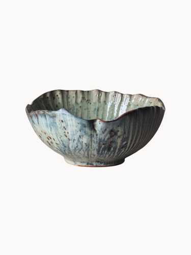 A rustic ceramic bowl with a mottled light blue and beige glaze with brown speckled details, on a plain white background.