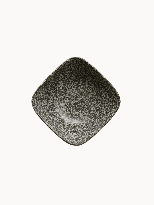 A top-down view on a ceramic bowl with a speckled black and white texture with subtle horizontal ribbed lines, on a plain white background. The deep bowl has a unique, square-like curved rim.