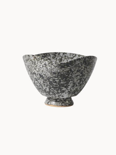 A ceramic bowl with a speckled black and white texture with subtle horizontal ribbed lines, on a plain white background. The deep bowl has a unique, square-like curved rim.