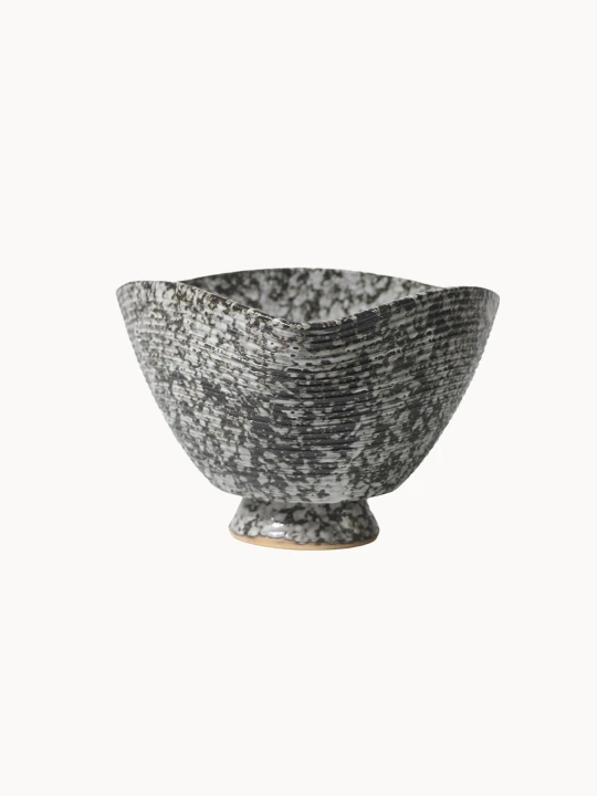 A ceramic bowl with a speckled black and white texture with subtle horizontal ribbed lines, on a plain white background. The deep bowl has a unique, square-like curved rim.