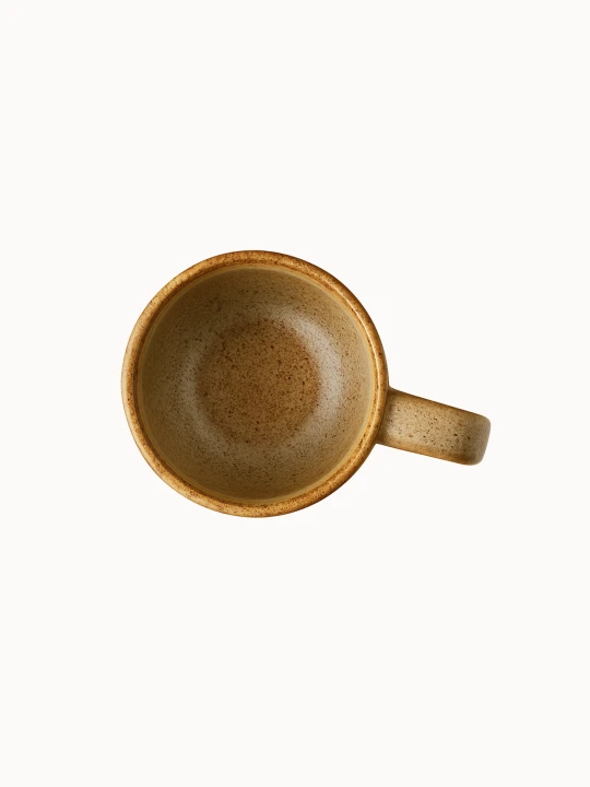 A top-down view on a speckled, light beige ceramic mug with a rounded shape and a sturdy handle is isolated on a plain white background.