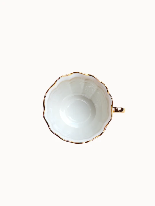 A top-down view on a porcelain teacup with an iridescent, pearlescent glaze displaying metallic blue, purple, and gold tones is isolated on a white background.