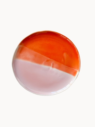 A top-down view on a ceramic cake stand, half glazed in glossy orange tone and half in a matte pastel pink.