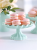 A stack of pink French macarons with white filling on a pastel blue cake stand. The stand is presented in a bright table setting with a blurred background.