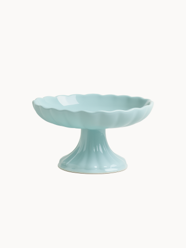 A pastel blue ceramic cake stand with a footed pedestal base and a scalloped, flower-like bowl with a wavy edge, on a light background.