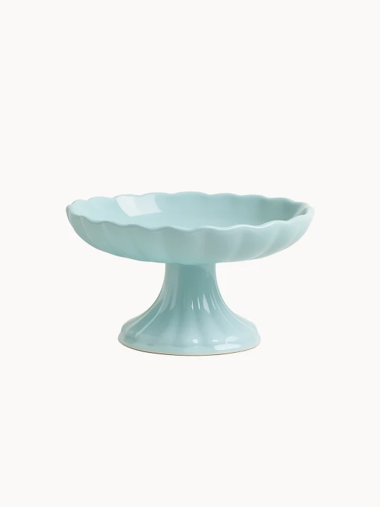 A pastel blue ceramic cake stand with a footed pedestal base and a scalloped, flower-like bowl with a wavy edge, on a light background.